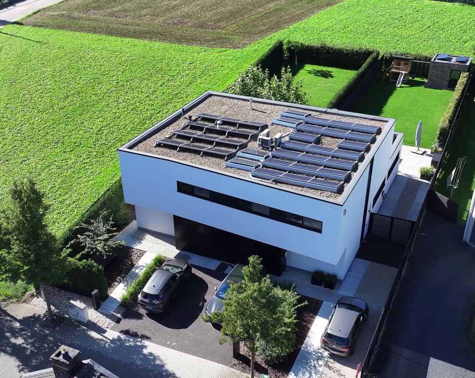 Dronefoto van de woning met het platte dak vol zonnepanelen, de oprit en de tuin